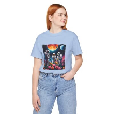 A chic woman wearing a baby blue colored T-shirt featuring a vibrant graphic of three astronauts in spacesuits watering colorful flowers under a celestial sky planets.