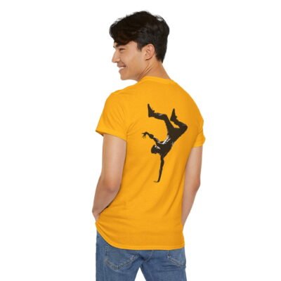 A young man wearing a gold colored T-shirt featuring a large black silhouette of a breakdancer doing a hand stand, centered stylishly on the back of the shirt.