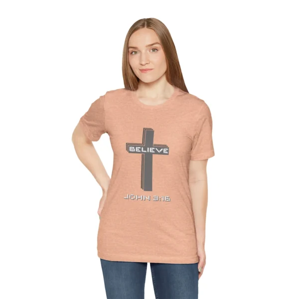 A female model wearing a Heather Peach colored "Believe 3:16", with a 3D stacked cross graphic and the words "Believe" and "John 3:16" on the front.