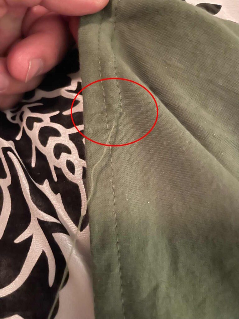 Another image of unsewn threads on a military green shirt. Again, there is a red circle that has been added to highlight the issue.