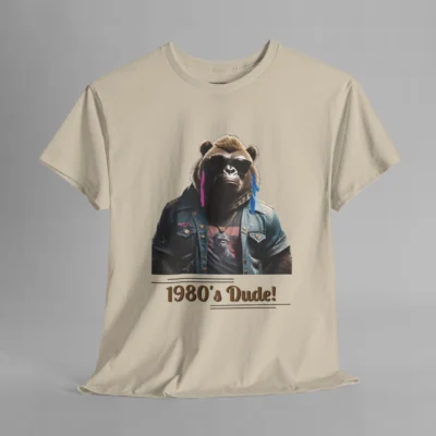A sand colored t-shirt mockup with one of our iconic gorilla-bear mascots, with pink and purple feather earrings, a swag jean jacket, dark shades, and a graphic tee underneath the jacket. The writing on the shirt says "1980's Dude!", bracketed inside of some horizontal lines.