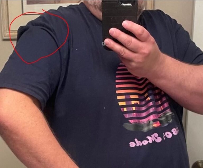 A person wearing a navy colored shirt, taking a picture in a mirror. There is a red circle highlighting issues with the fit of the garment's sleeve.