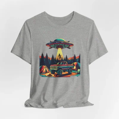 Athletic heather colored t-shirt mockup of a camping scene, with a 1980 style pick-up truck, tents, and an alien space ship in the background, abducting a Big Foot looking creature from out of a pine forest. Colors are red, orange, blue, and yellow.