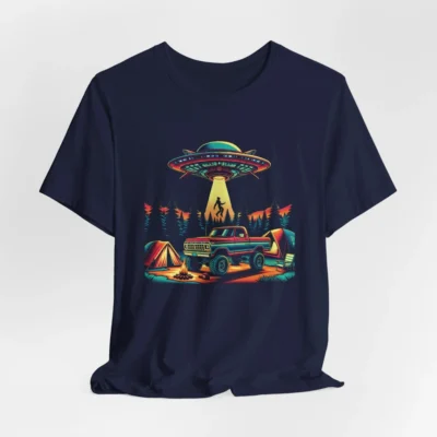 Navy colored t-shirt mockup of a camping scene, with a 1980 style pick-up truck, tents, and an alien space ship in the background, abducting a Big Foot looking creature from out of a pine forest. Colors are red, orange, blue, and yellow.