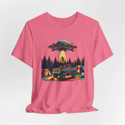 Pink colored t-shirt mockup of a camping scene, with a 1980 style pick-up truck, tents, and an alien space ship in the background, abducting a Big Foot looking creature from out of a pine forest. Colors are red, orange, blue, and yellow.
