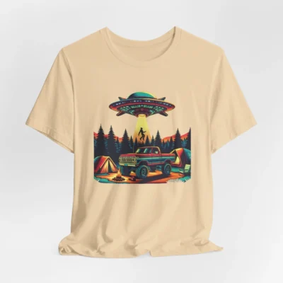 Soft cream colored t-shirt mockup of a camping scene, with a 1980 style pick-up truck, tents, and an alien space ship in the background, abducting a Big Foot looking creature from out of a pine forest. Colors are red, orange, blue, and yellow.