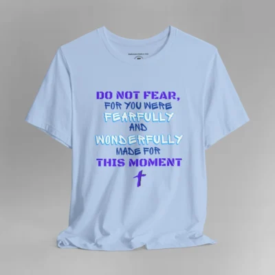 A baby blue colored tee with the words "Do Not Fear, For You Were Fearfully and Wonderfully Made For This Moment" in varying fonts and colors (purple, deep blue, and light aqua blue). There is a graphic, artistic purple cross beneath the words.