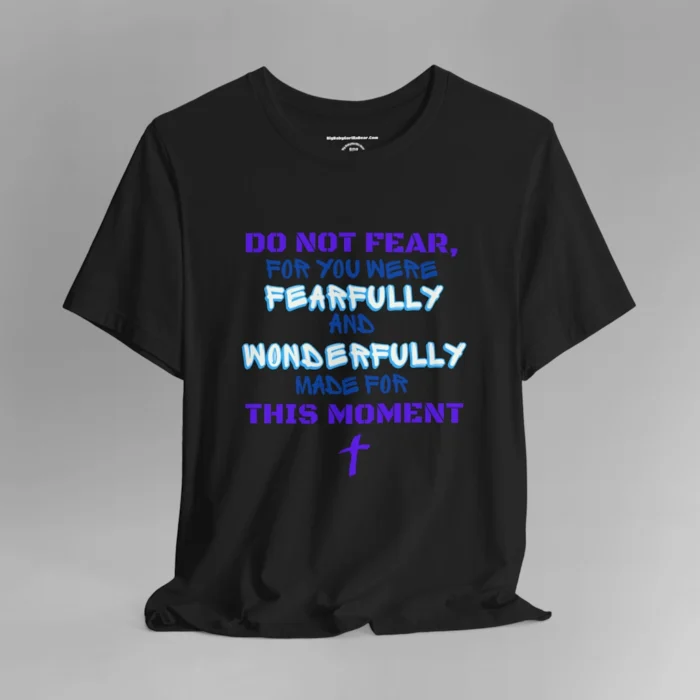 A black colored tee with the words "Do Not Fear, For You Were Fearfully and Wonderfully Made For This Moment" in varying fonts and colors (purple, deep blue, and light aqua blue). There is a graphic, artistic purple cross beneath the words.