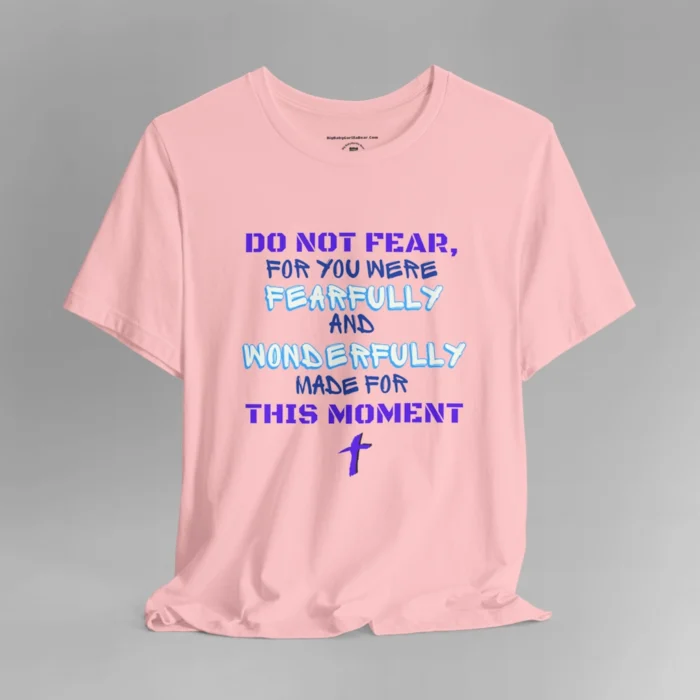 A pink colored tee with the words "Do Not Fear, For You Were Fearfully and Wonderfully Made For This Moment" in varying fonts and colors (purple, deep blue, and light aqua blue). There is a graphic, artistic purple cross beneath the words.