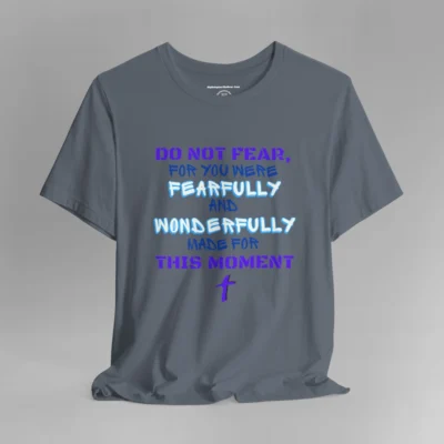 A steel blue colored tee with the words "Do Not Fear, For You Were Fearfully and Wonderfully Made For This Moment" in varying fonts and colors (purple, deep blue, and light aqua blue). There is a graphic, artistic purple cross beneath the words.