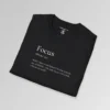 Black folded t-shirt mockup with the word "Focus" on the front, in the appearance of a word in a dictionary, including pronunciation beneath the main word. The text beneath says "WAIT...does it say Hokus? Oh, that reminds me of MAGIC...Oh, yeah, focus...OH LOOK, a fly on the wall!!!!"