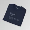 Navy folded t-shirt mockup with the word "Focus" on the front, in the appearance of a word in a dictionary, including pronunciation beneath the main word. The text beneath says "WAIT...does it say Hokus? Oh, that reminds me of MAGIC...Oh, yeah, focus...OH LOOK, a fly on the wall!!!!"