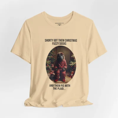 Vertical Layout of a tee showcasing the "Shorty PJs With the Plaid" BigBabyGorillaBear.Com Soft Cream colored graphic tee! This tee has a Big Baby Gorilla Bear with plaid PJs and fuzzy socks in a Christmas scene, with the words "Shorty Got Them Christmas Fuzzy Socks and Them PJs with the Plaid..."