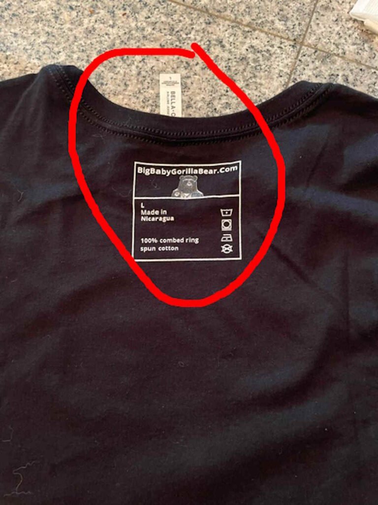 An example defect image that shows the inside product label was printed on the outside of the shirt. The inner tag is flipped up to illustrate the inner tag area.