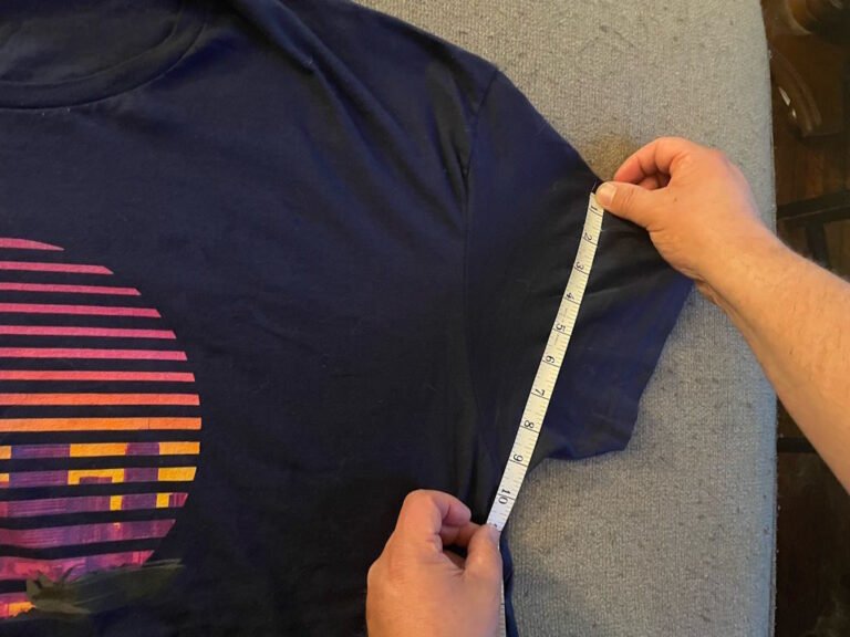 An image of a tape measure, and a person's hands measuring the sleeves of a navy colored t-shirt.