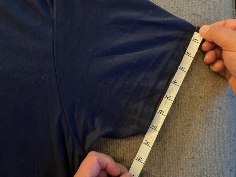 A close up of a measuring tape on the end of the sleeve of a navy shirt. The tape measure and measurements are clearly visible.