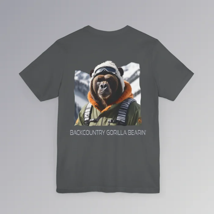 An asphalt colored tee with a backside graphic of one of our iconic gorilla grizzly bears, fully dressed in an army/olive colored snow jacket with orange trim, white toboggan, and a backpack. There are snowy mountains in the background. Beneath the image is text that reads "Backcountry Gorilla Bearin'".