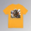 An gold colored tee with a backside graphic of one of our iconic gorilla grizzly bears, fully dressed in an army/olive colored snow jacket with orange trim, white toboggan, and a backpack. There are snowy mountains in the background. Beneath the image is text that reads "Backcountry Gorilla Bearin'".