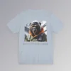 An light blue colored tee with a backside graphic of one of our iconic gorilla grizzly bears, fully dressed in an army/olive colored snow jacket with orange trim, white toboggan, and a backpack. There are snowy mountains in the background. Beneath the image is text that reads "Backcountry Gorilla Bearin'".