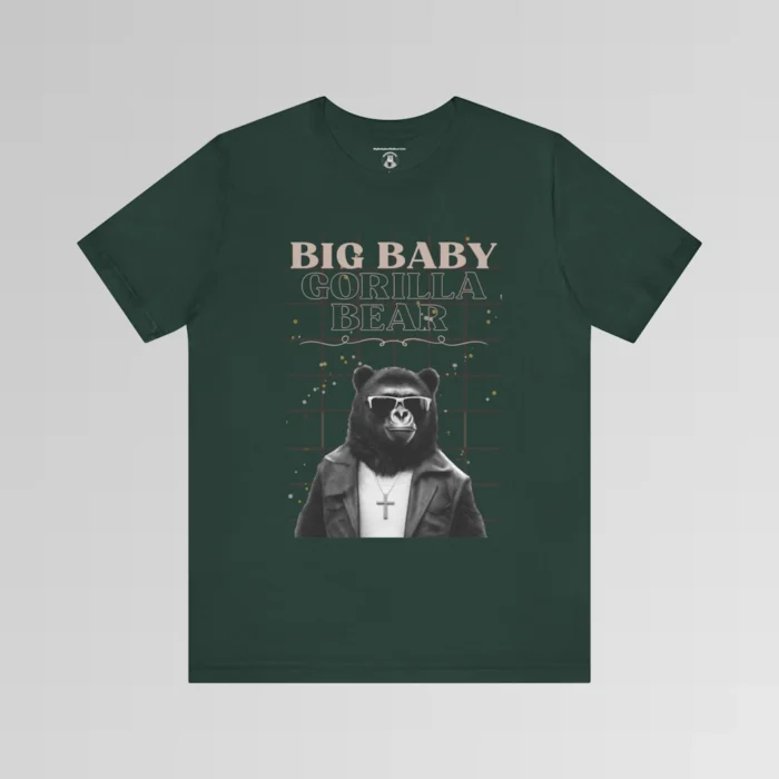 A forest green t-shirt mockup with our iconic grizzly bear and gorilla hybrid, wearing a leather jacket, cross necklace, and shades. The background of the shirt has a grid and some confetti. The words above the image are "Big Baby Gorilla Bear in two fonts, with a decorative ribbon separating the words from the mascot image. Retro look with tan, black, grey, and white colors.