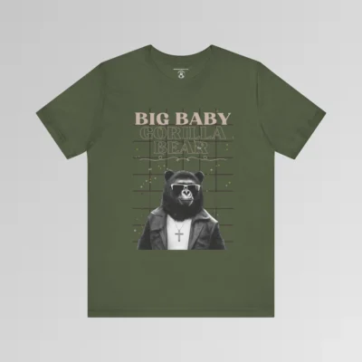 A military green t-shirt mockup with our iconic grizzly bear and gorilla hybrid, wearing a leather jacket, cross necklace, and shades. The background of the shirt has a grid and some confetti. The words above the image are "Big Baby Gorilla Bear in two fonts, with a decorative ribbon separating the words from the mascot image. Retro look with tan, black, grey, and white colors.