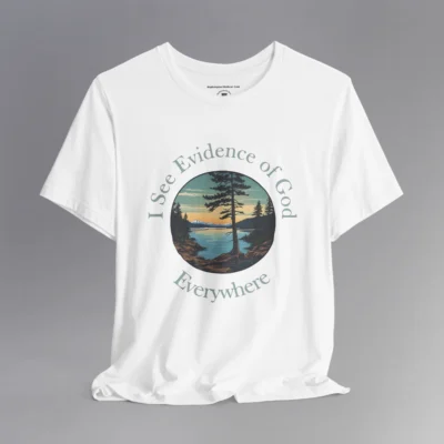 A white t-shirt with a cove on a lake, and a slightly off centered focal point pine tree, with mountains in the distance, and pine trees on the edge of the circular graphic. The sun is setting in the image. Text around the image says "I See Evidence of God" on the top half, and "Everywhere" on the bottom half; text wrapped around the image.