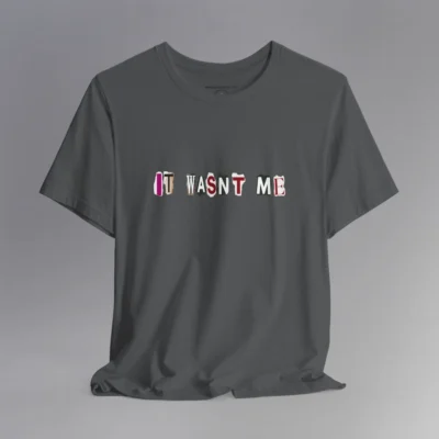 An asphalt tee with magazine cutout letters of various fonts and colors arranged to spell out "It Wasn't Me", on the front of the t-shirt.