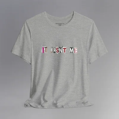 An athletic heather tee with magazine cutout letters of various fonts and colors arranged to spell out "It Wasn't Me", on the front of the t-shirt.