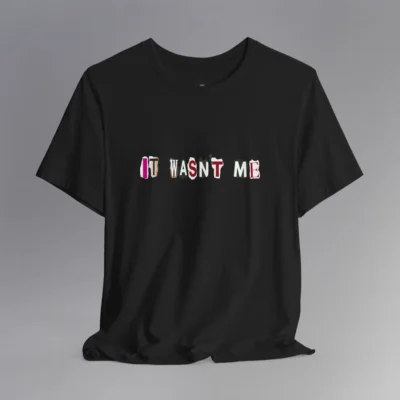 A black tee with magazine cutout letters of various fonts and colors arranged to spell out "It Wasn't Me", on the front of the t-shirt.