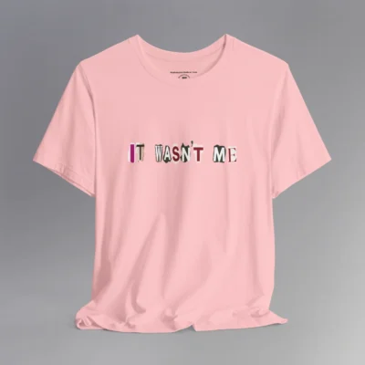 A pink tee with magazine cutout letters of various fonts and colors arranged to spell out "It Wasn't Me", on the front of the t-shirt.