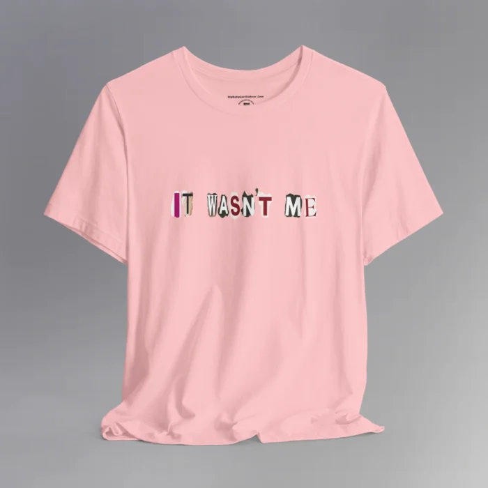 A pink tee with magazine cutout letters of various fonts and colors arranged to spell out "It Wasn't Me", on the front of the t-shirt.