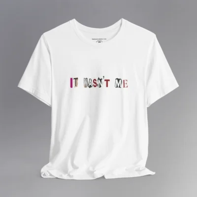 A white tee with magazine cutout letters of various fonts and colors arranged to spell out "It Wasn't Me", on the front of the t-shirt.