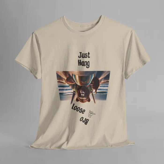 A sand colored graphic tee with one of our iconic bear-gorilla hybrid creatures riding on top of a fighter over a beach. The image is turned upside down, and in the shape of an upside down trapezoid. Above the image is writing that says " Just Hang", and beneath the image it says "Loose Bro" at an angle, and with a hang-loose hand gesture clip art.