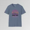 A heather indigo shirt with a view of the Miami, FL skyline (not necessarily an accurate view), with a blind effect, as if it appears as if the viewer is looking through window blinds. At the bottom is a generic 1980's style convertible, and a speed boat. Beneath the image says "1980's Mode" . The image has pinks, oranges, greys, purples, and some yellows.