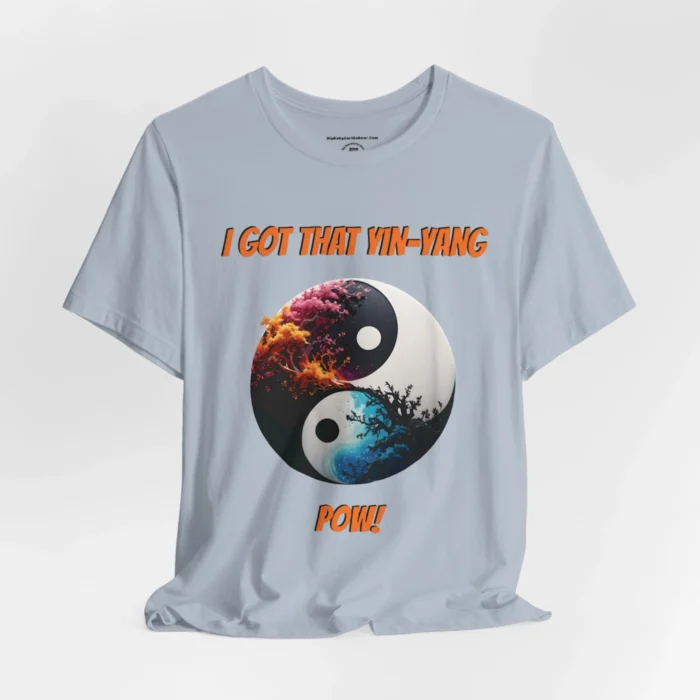 An light blue t-shirt with a Black and white yin-yang, that appears to have trees growing out of the center. The trees are orang and pink, and blacked out. The bottom part of the yin-yang has blue swirls. "I Got That Yin-Yang" is above the image. "Pow!" is beneath the image. The graphic is on the front of the shirt.