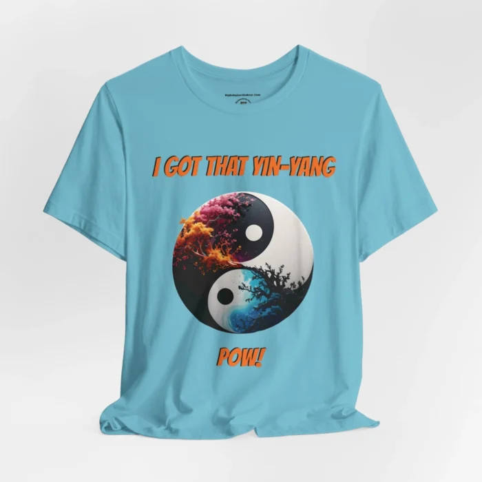 An turquoise t-shirt with a Black and white yin-yang, that appears to have trees growing out of the center. The trees are orang and pink, and blacked out. The bottom part of the yin-yang has blue swirls. "I Got That Yin-Yang" is above the image. "Pow!" is beneath the image. The graphic is on the front of the shirt.