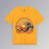 The frontside of a gold colored t-shirt with an oriental feel, and a blue wave white-capping, with a sunset in the background. The wave looks as if it touches the sun. There are mountains, clouds, and gentle waves, with hues of orange, red, and yellows.