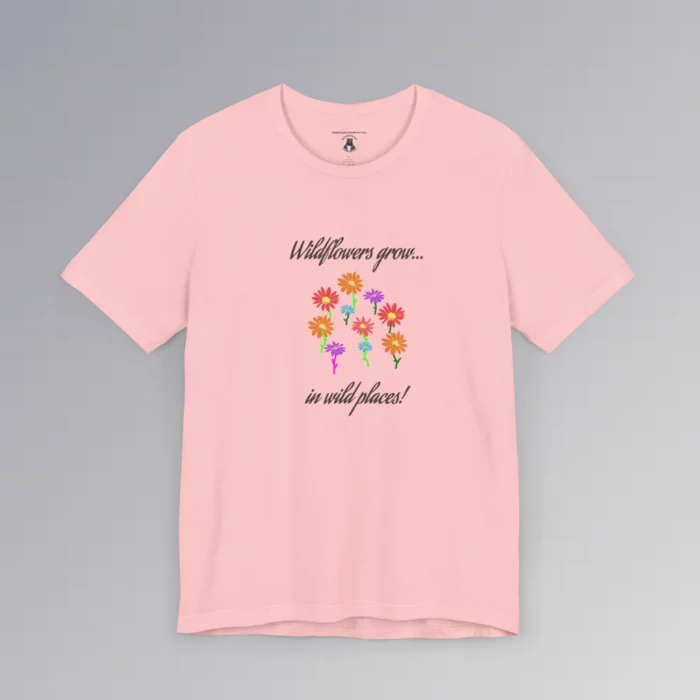 Pink colored t-shirt with blue, red, orange, and purple coneflower-like flowers, with green and mauve colored stems. In a handwriting font, is says "Wildflowers grow..." above the flowers, and "in wild places!" beneath the flowers.