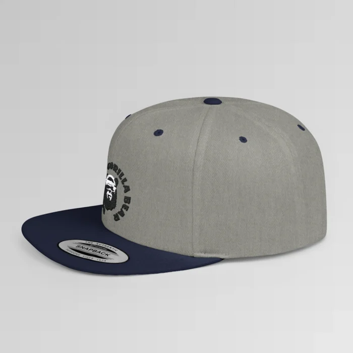 A mockup of a side view of the "BBGB Flat Bill Snapback Cap", with "Big Baby Gorilla Bear" embroidered in a circular font pattern surrounding the Big Baby Gorilla Bear Mascot embroidered on a navy cap.