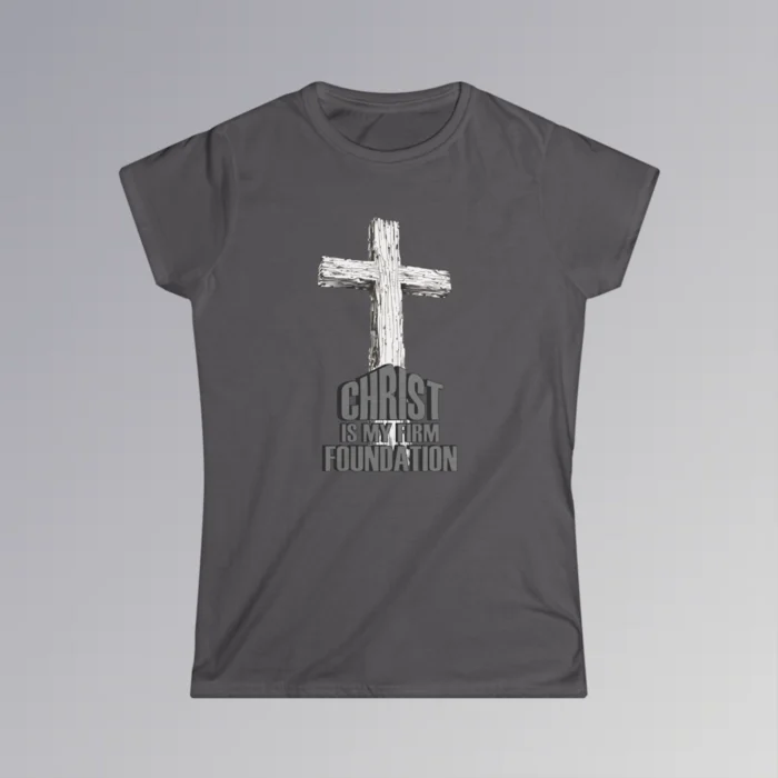 The front of a t-shirt with 3D text which states "Christ Is My Firm Foundation", from a slightly left perspective, in the shape of a simple house, with an old, wooden cross in the background. Color: Charcoal. Her Style.