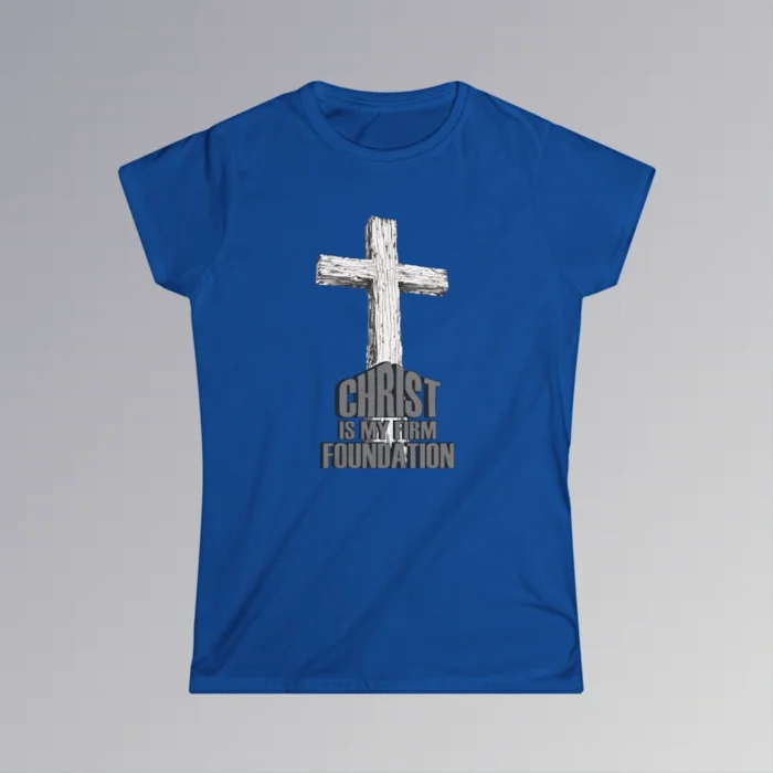 The front of a t-shirt with 3D text which states "Christ Is My Firm Foundation", from a slightly left perspective, in the shape of a simple house, with an old, wooden cross in the background. Color: Royal. Her Style.