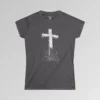 The front of a t-shirt with 3D text which states "The Rock On Which I Stand", from a slightly left perspective, in the shape of a simple house, with an old, wooden cross in the background. Color: Charcoal. Her Style.