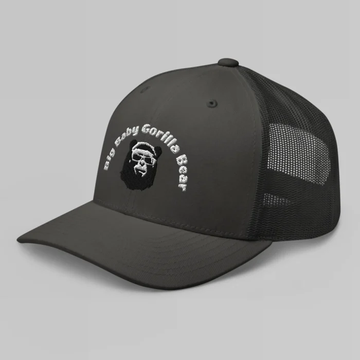 Left side view of a Charcoal mesh trucker cap, with the Big Baby Gorilla Bear mascot's face and the Big Baby Gorilla Bear Name Embroidered in black and white on the front of the cap.
