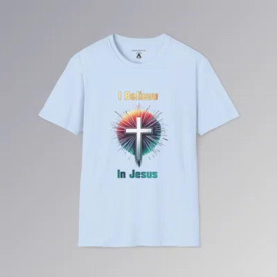 A light blue colored t-shirt with the words "I Believe" and "In Jesus" above and below a Christian cross, with a gradient white to very light blue filling the cross.. Around the cross is a vibrant circle with lines like stars shooting out, in the colors ranging from yellow to orange, pink, to teal and blue. The words "I Believe" has a gradient fill color of yellow to orange. The words "In Jesus" has a gradient fill color of teal to dark teal/blue.