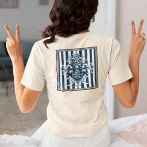 A female model showcasing the back of the "BBGB Crest Graphic T-shirt", sitting on a bed, holding both hands up showing peace signs with her fingers.