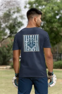 A male model showcasing the "BBGB Crest Graphic T-shirt" (Navy colored), wearing padded sport gloves and standing on a playing field.