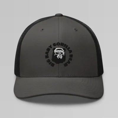 Front side view of a Charcoal Black mesh trucker cap, with the Big Baby Gorilla Bear mascot's face and the Big Baby Gorilla Bear Name encircling the face, Embroidered in black and white on the front of the cap.
