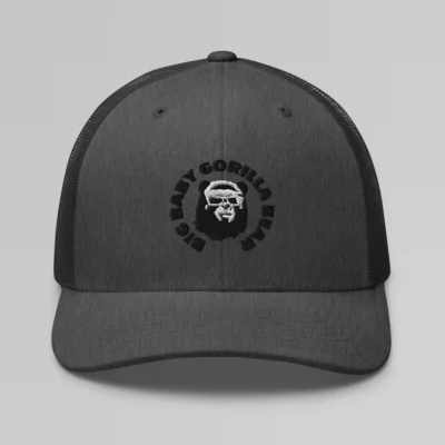 Front side view of a Dark Heather mesh trucker cap, with the Big Baby Gorilla Bear mascot's face and the Big Baby Gorilla Bear Name encircling the face, Embroidered in black and white on the front of the cap.