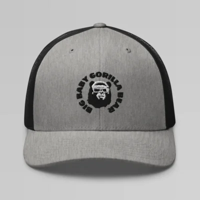 Front side view of a Heather Black mesh trucker cap, with the Big Baby Gorilla Bear mascot's face and the Big Baby Gorilla Bear Name encircling the face, Embroidered in black and white on the front of the cap.