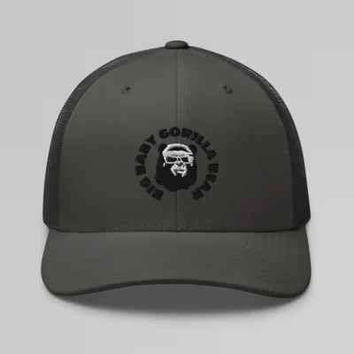 Front side view of a Charcoal mesh trucker cap, with the Big Baby Gorilla Bear mascot's face and the Big Baby Gorilla Bear Name encircling the face, Embroidered in black and white on the front of the cap.